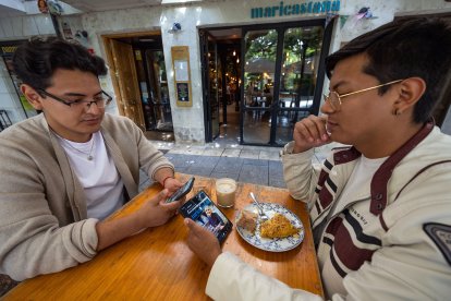 Dos clientes consultan en su teléfono móvil información sobre el local de hostelería en el que están consumiendo.