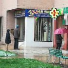 Compradores hacen cola frente a una farmacia esta mañana bajo la lluvia esperando a ser atendidos, dejando más de un metro de distancia. S. L. C.