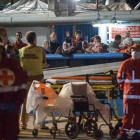 Los inmigrantes supervivientes de un naufragio llegan este jueves a tierra firme tras ser salvados por las autoridades de Libia, mientras los equipos médicos se llevan los cuerpos de los fallecidos.-REX SHUTTERSTOCK/ANTONIO MELITA