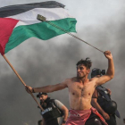Un joven palestino tira piedras con una honda mientras con la otra mano lleva la bandera palestina.-MUSTAFA HASSONA / GETTY IMAGES