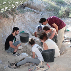 Dos de los excavadores trabajan con la brocha para limpiar un fósil.-CAS