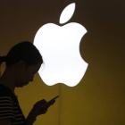 Una mujer mira su teléfono ante el logo de Apple en la tienda oficial de Shangai, China.-Foto: REUTERS / ALY SONG