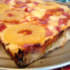 Una porción de pizza hawaiana, con rodajas de piña enteras.-