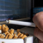 Detalle de un cenicero lleno de colillas mientras una persona sostiene un cigarro. SANTI OTERO