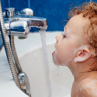 Un niño trata de beber agua del grifo  de la bañera.-EL MUNDO