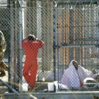 Un recluso de Guantánamo, escoltado por dos guardias en el penal, junto a otros dos presos en sus celdas, el 15 de marzo del 2002.-AP / TOMAS VAN HOUTRYVE