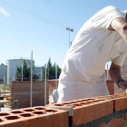 Un albañil trabaja levantando una pared en una obra junto con otros profesionales de la construcción.-ICAL