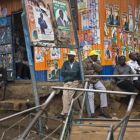 Un grupo de kenianos junto a un local con la fachada cubierta de carteles durante la campaña electoral-AP / JEROME DELAY