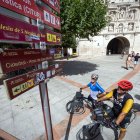 Unos ciclistas se interesan por la señalización turística, en un poste que tiene distintos tipos de letreros.