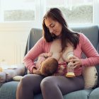 Una madre da pecho a su hijo mientras se saca leche.