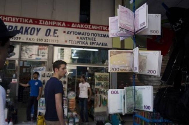 Ciudadanos griegos pasean ante carteras con el diseño del euro en un quiosco del centro de Atenas, este martes.-