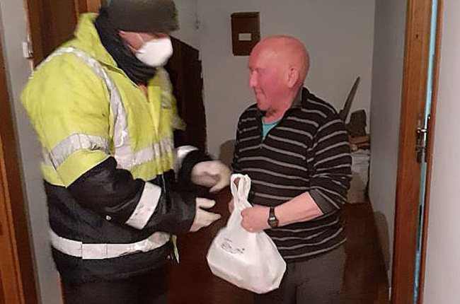 Un voluntario protegido con mascarilla y guantes entrega comida a un hombre mayor en Quintanar de la Sierra. ECB