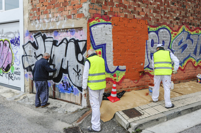 Trabajadores de los planes de empleo, de anteriores ejercicios, limpiando una pintada vandálica.