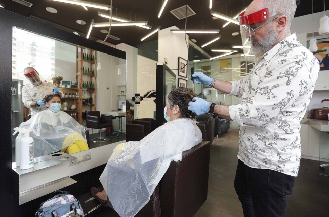 Un profesional atiende a una clienta en una peluquería, ambos protegidos para prevenir el contagio del Covid. ECB