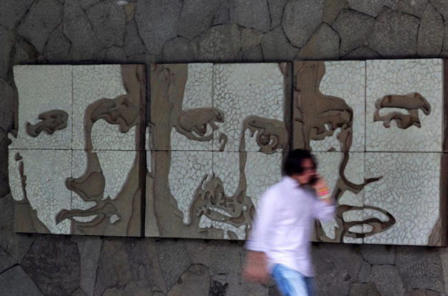 Un hombre pasa frente a un muro con los retratos de tres de los seis jesuitas asesinados en El Salvador en 1989, este miércoles.-REUTERS / JOSÉ CABEZAS