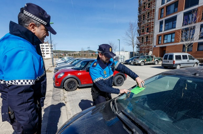 Dos agentes de la Policía Local de Burgos colocan una pegatina verde en un coche que podría estar abandonado. SANTI OTERO