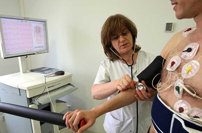 Una enfermera toma la tensión a un paciente que se somete a un electrocardiograma.-ICAL