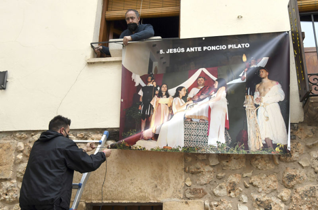 Dos personas colocan una de las lonas con las fotos de la Semana Santa de Covarrubias. ICAL