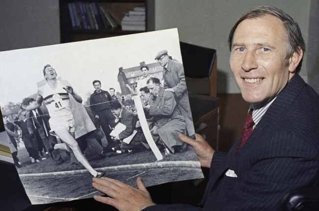 Roger Bannister, en una imagen de 1974, mostrando una foto de 20 años antes batiendo el récord de la milla.-AFP