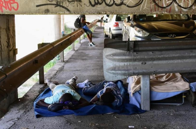 Unos inmigrantes tratan de descansar en el párking ubicado bajo un puente en la localidad italiana de Ventimiglia.-MIGUEL MEDINA (AFP)