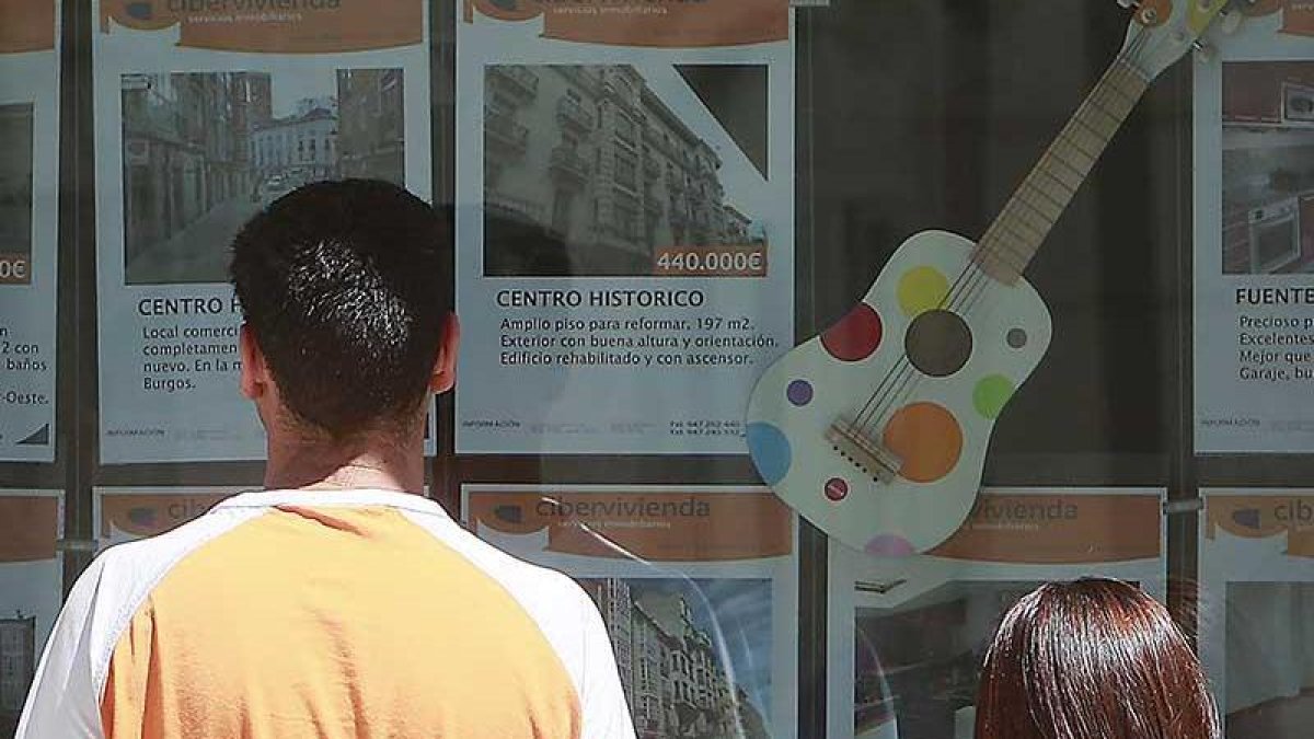 Dos jóvenes observan ofertas de pisos en una inmobiliaria.