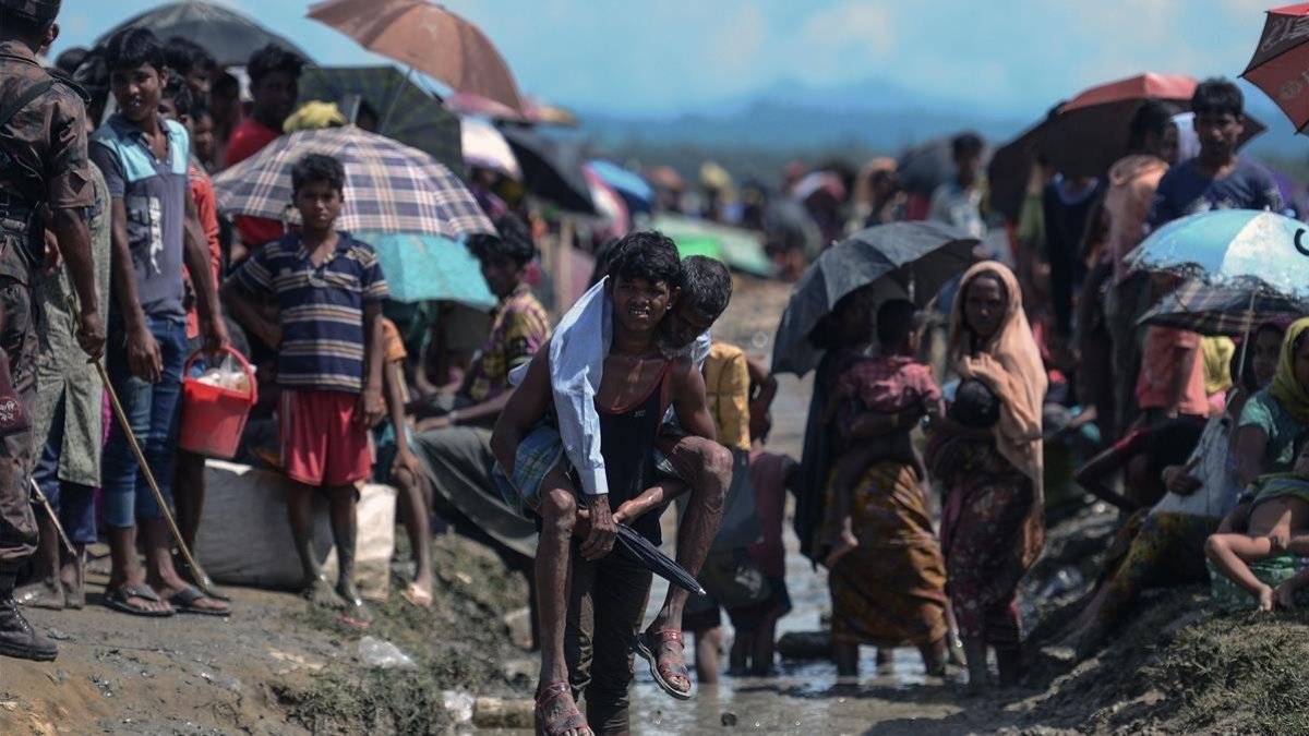Un refugiado rohinyá lleva a cuestas a un anciano en Bangladés, cerca de la frontera con Birmania-AFP