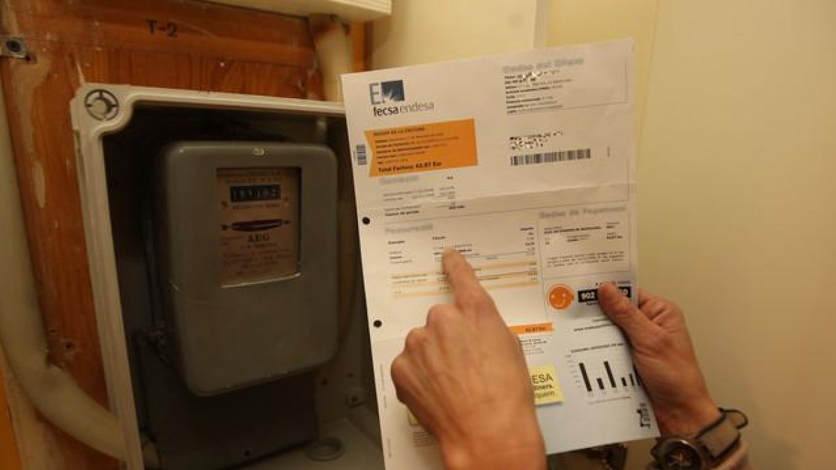 Una mujer consulta una factura de la luz frente al contador de su casa.