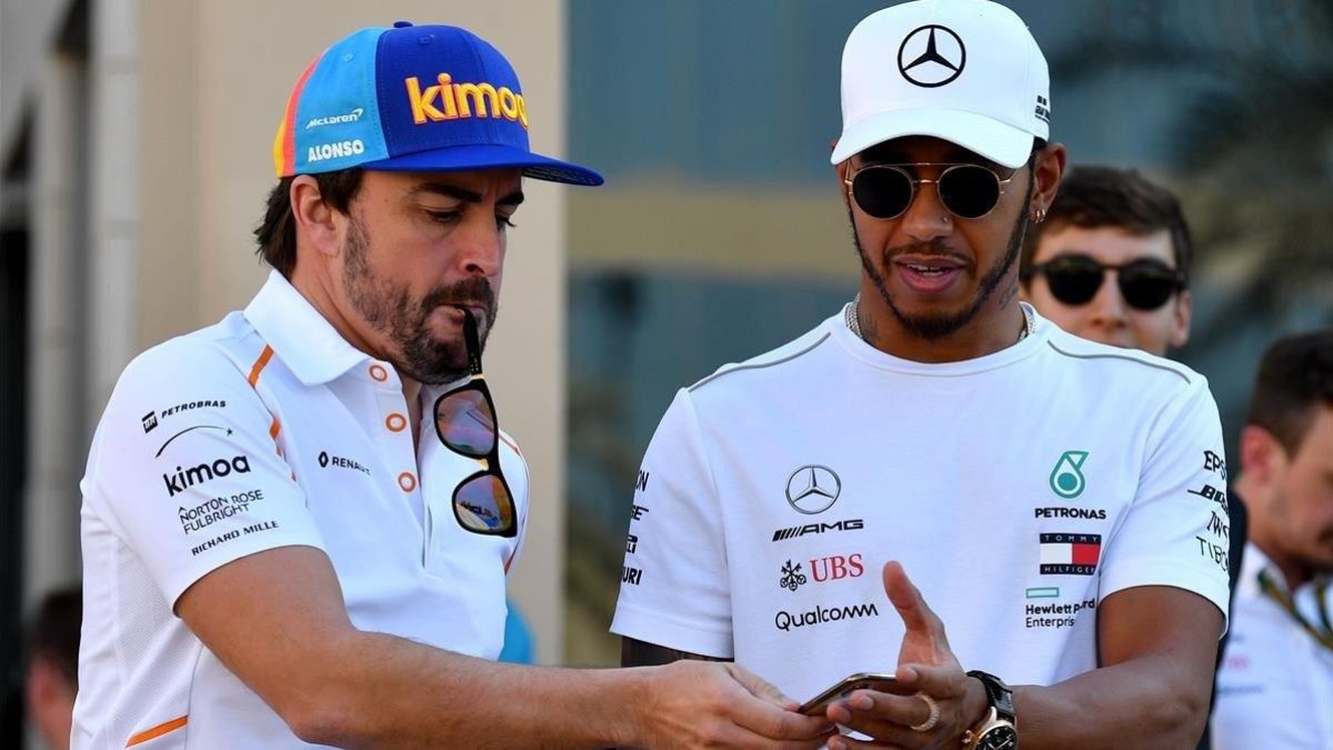 Alonso consulta un móvil junto a Hamilton en Abu Dhabi.-AFP