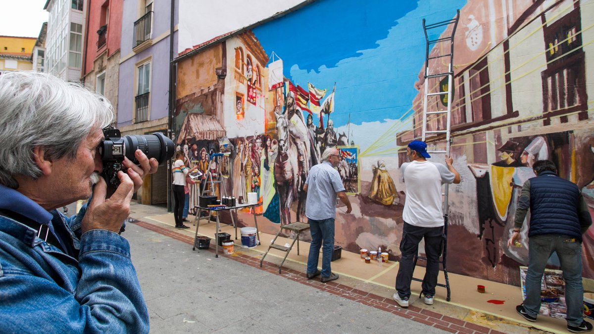 Un hombre hace una fotografía al mural mientras los artistas trabajan en él. TOMÁS ALONSO