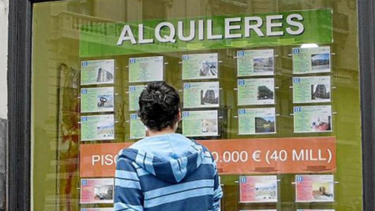 Un joven mira anuncios de viviendas en alquiler en el escaparate de una inmobiliaria. ECB