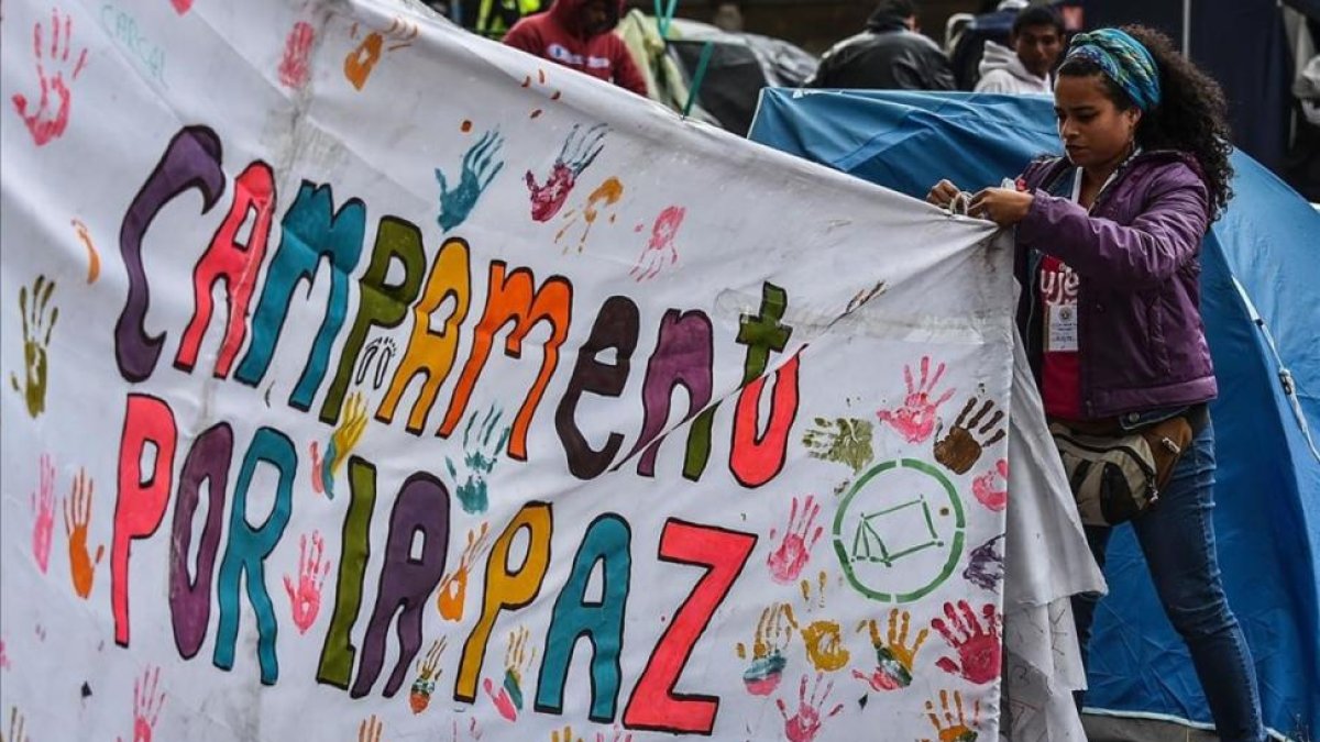Una joven ayuda a colocar una pancarta a favor del acuerdo de paz en la acampada de la plaza Bolivar, en Bogotá.-AFP / LUIS ACOSTA