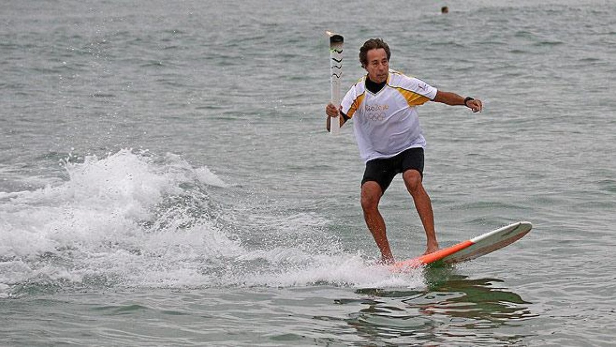 La antorcha olímpica surfea en las playas de Río.-AP / CHARLIE RIEDEL