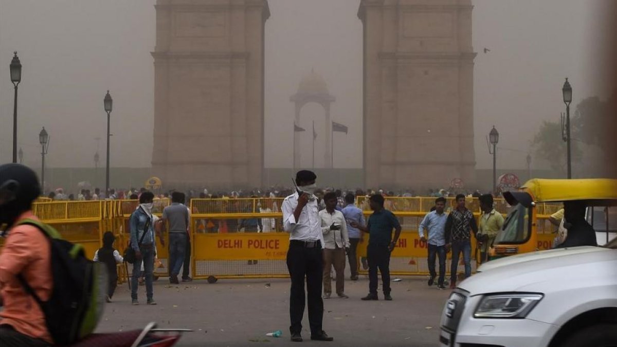 Un agente de policía de Nueva Delhi dirige el tráfico mientras se cubre la cara en medio de una tormenta de arena.-/ CHANDAN KHANNA (AFP)