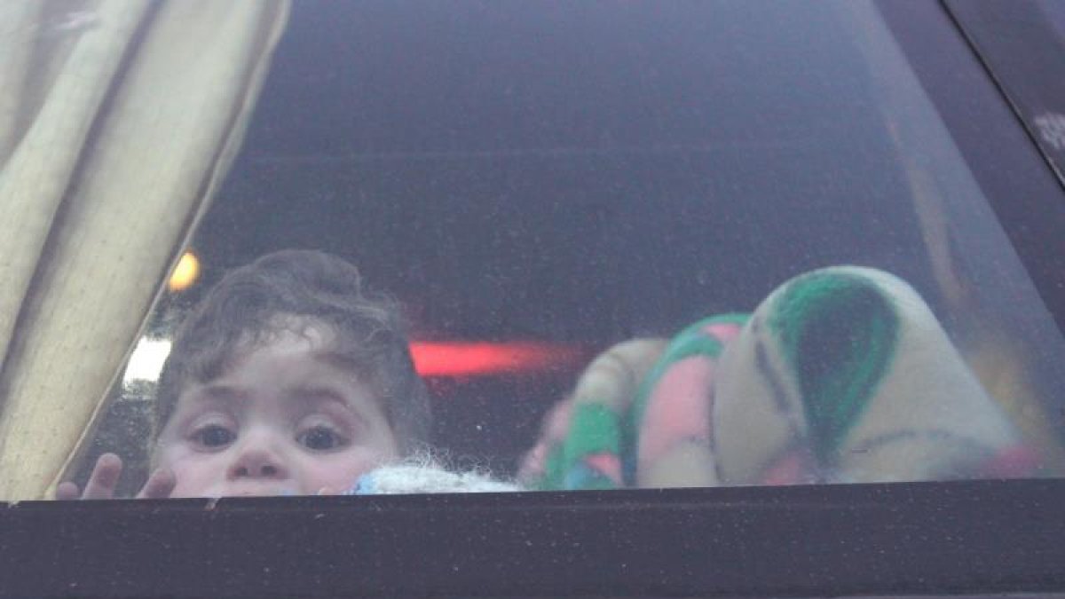 n niño mira por la ventana de un autobús la llegada de civiles y combatientes a la localidad de Qalaat al-Madiq, al sudeste de la ciudad tomada por los rebeldes de Idlib (Siria).-EFE