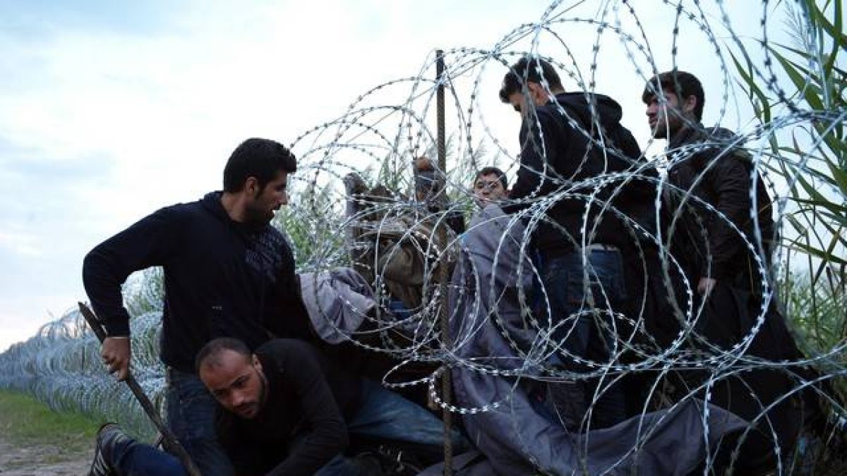 Refugiados sirios cruzan la alambrada de espino situada por las autoridades húngaras en su frontera.-Bela Szandelszky/AP/BEA SZANDELSKY