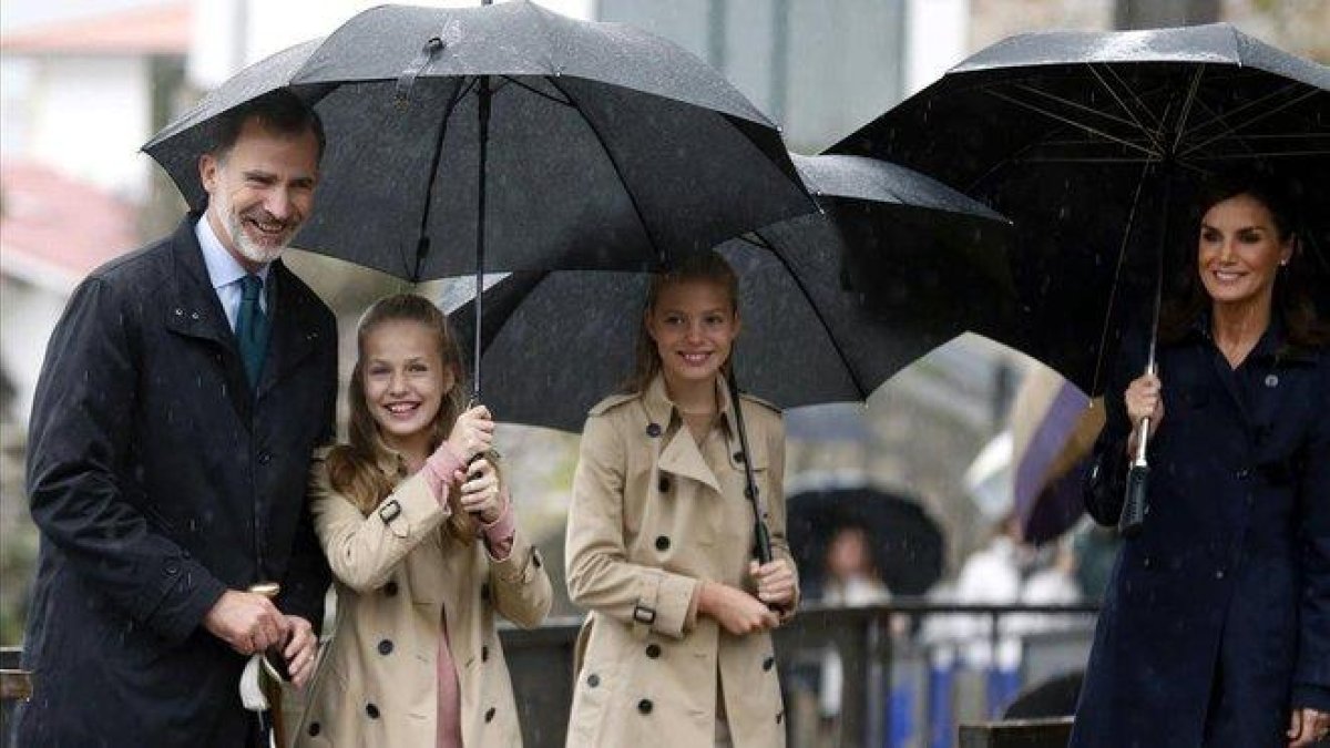 El rey Felipe VI, la princesa Leonor, la infanta Sofía y la reina Letizia, bajo la lluvia, en su visita a Asiegu (Asturias).-EFE/ L. CEREIJIDO