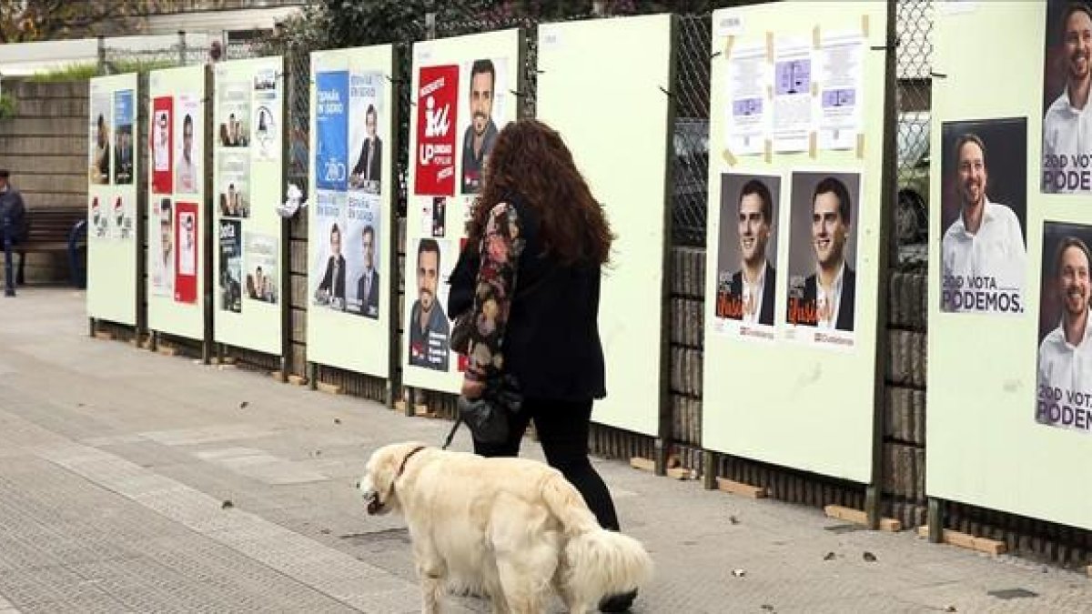 Una mujer pasea tranquilamente con su perro ante los carteles electorales, en Bilbao.-LUIS TEJIDO / EFE