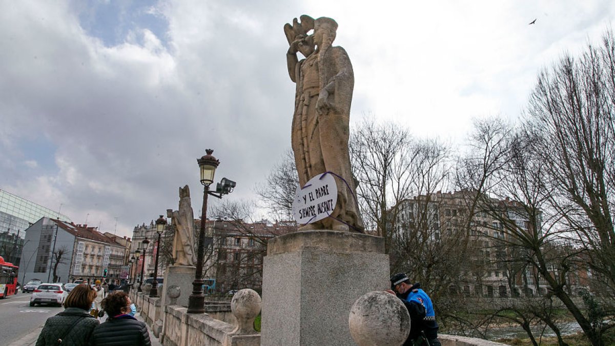Un policía local corta la cuerda que sujetaba uno de los carteles en las estatuas del puente de San Pablo. TOMÁS ALONSO