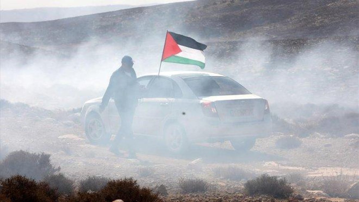 Un hombre ondea la bandera palestina entre gas lacrimogeno en el pueblo cisjordano de Shiyoukh.-ABED AL HASHLAMOUN (EFE)