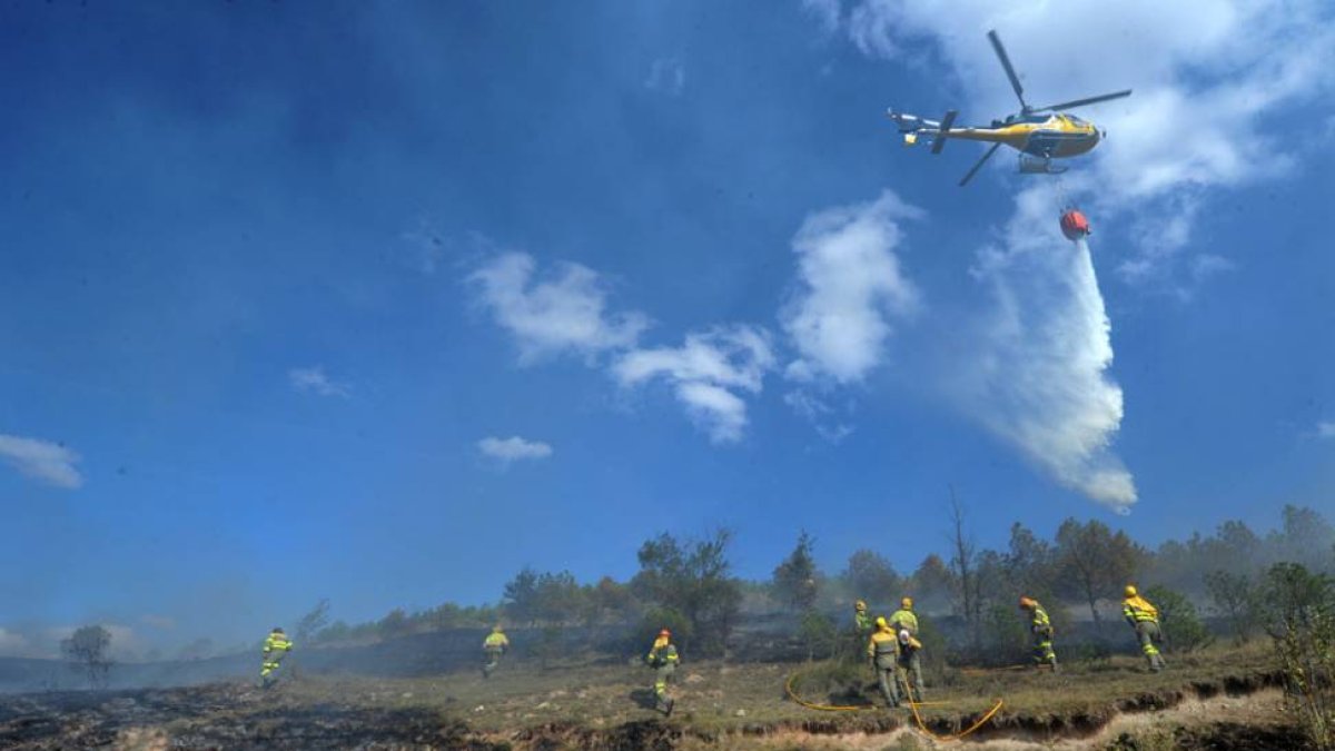 Un helicóptero descarga agua mientras las cuadrillas de tierra trabajan sobre el terreno.-ISRAEL L. MURILLO