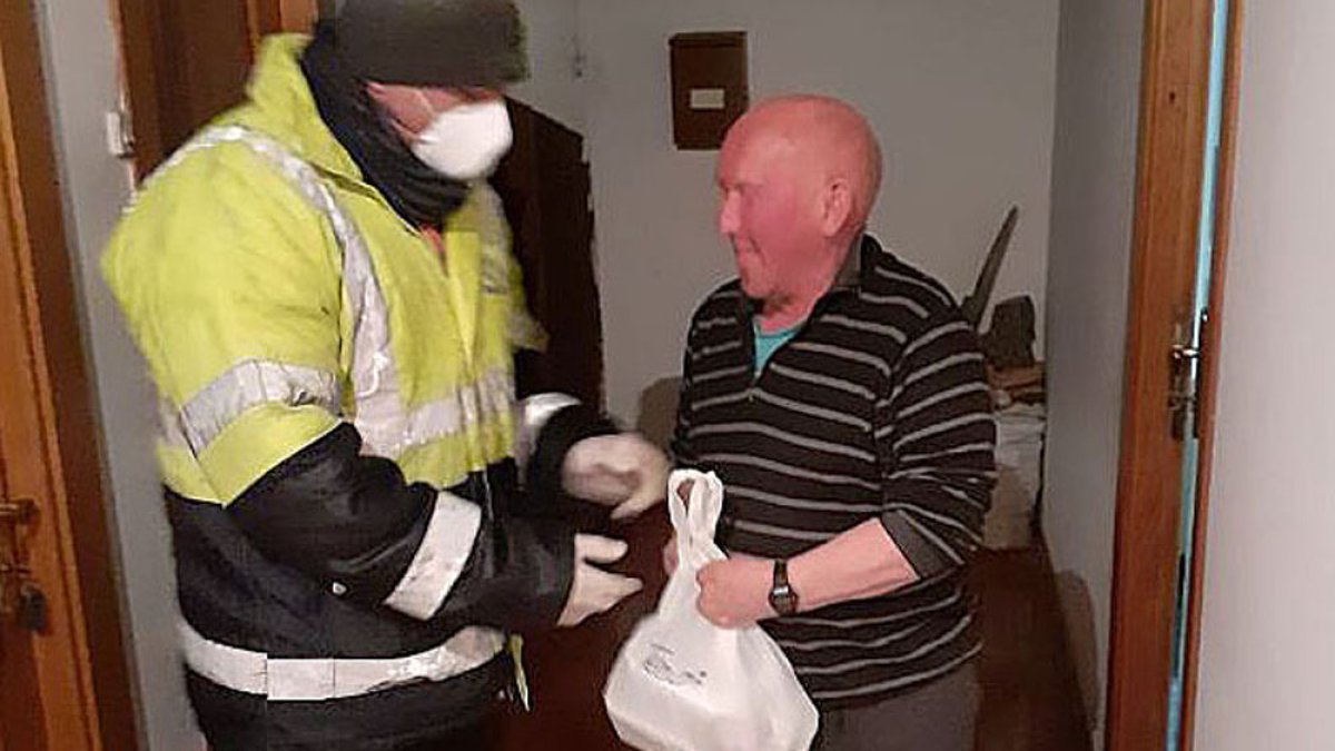 Un voluntario protegido con mascarilla y guantes entrega comida a un hombre mayor en Quintanar de la Sierra. ECB