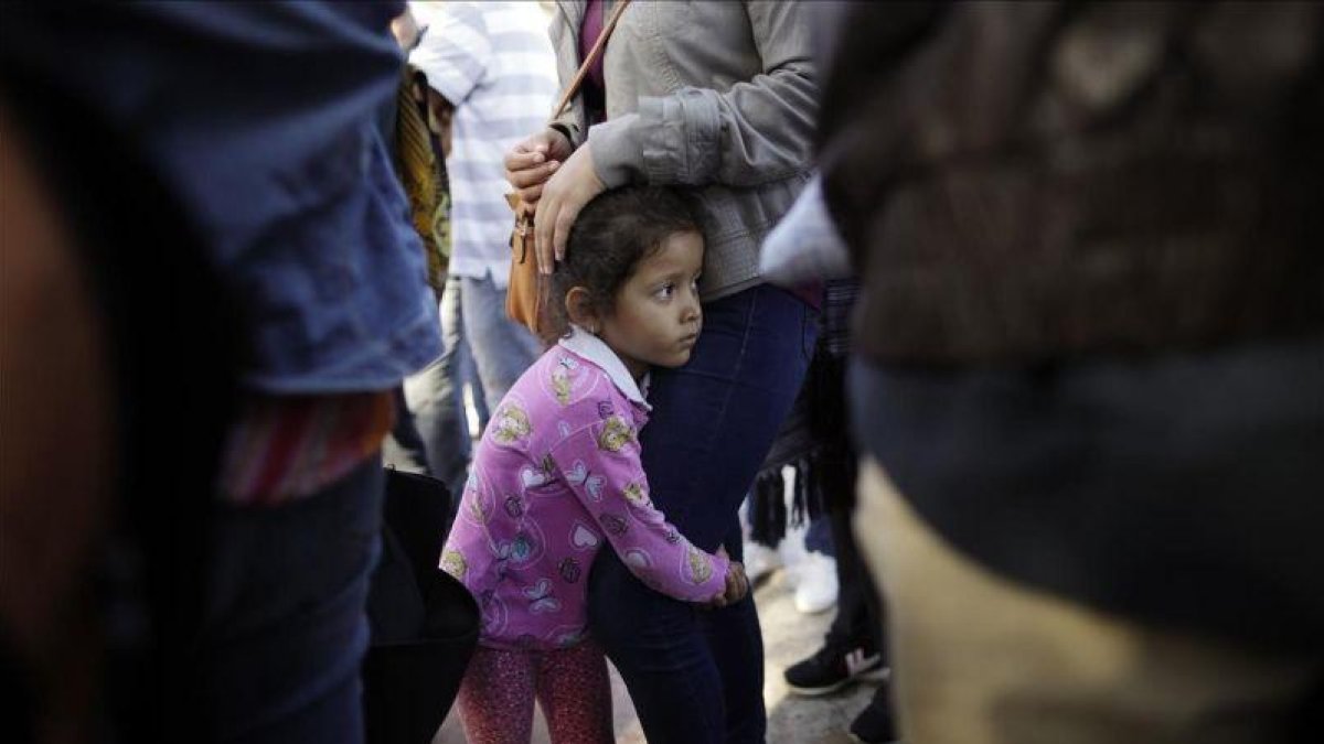 Una niña mexicana con su madre espera con otros inmigrantes en la frontera la respuesta a la solicitud de asilo político en EEUU.-GREGORY BULL (AP)