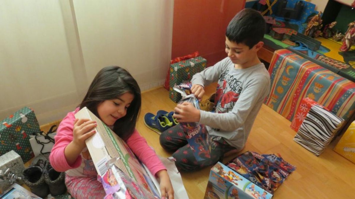 Dos hermanos disfrutan abriendo sus regalos de Reyes.-ECB
