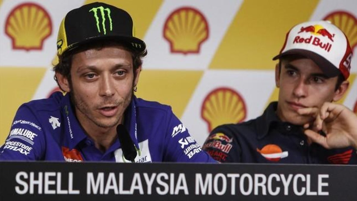 Valentino Rossi explica sus sensaciones antes del Gran Premio de Malasia, bajo la atenta mirada de Marc Márquez.-AP / JOSHUA PAUL