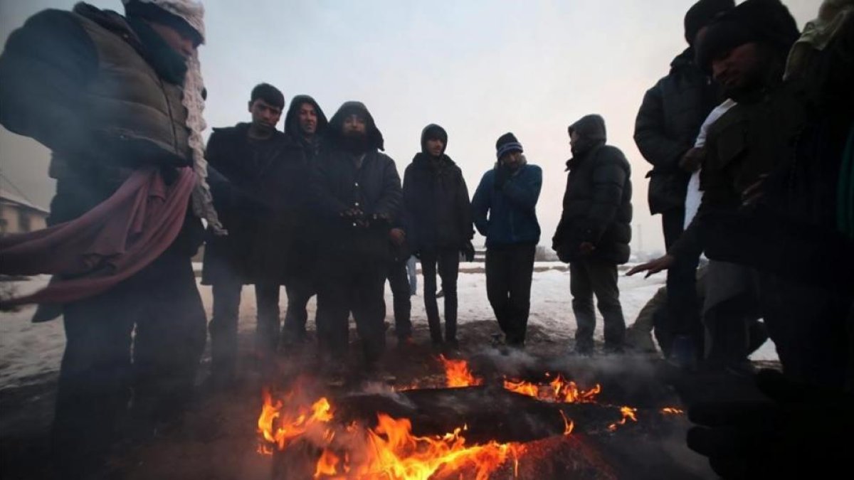 Un grupo de refugiados se protege del frio en Bergrado, Serbia.-EFE / ULEJMANOVIC