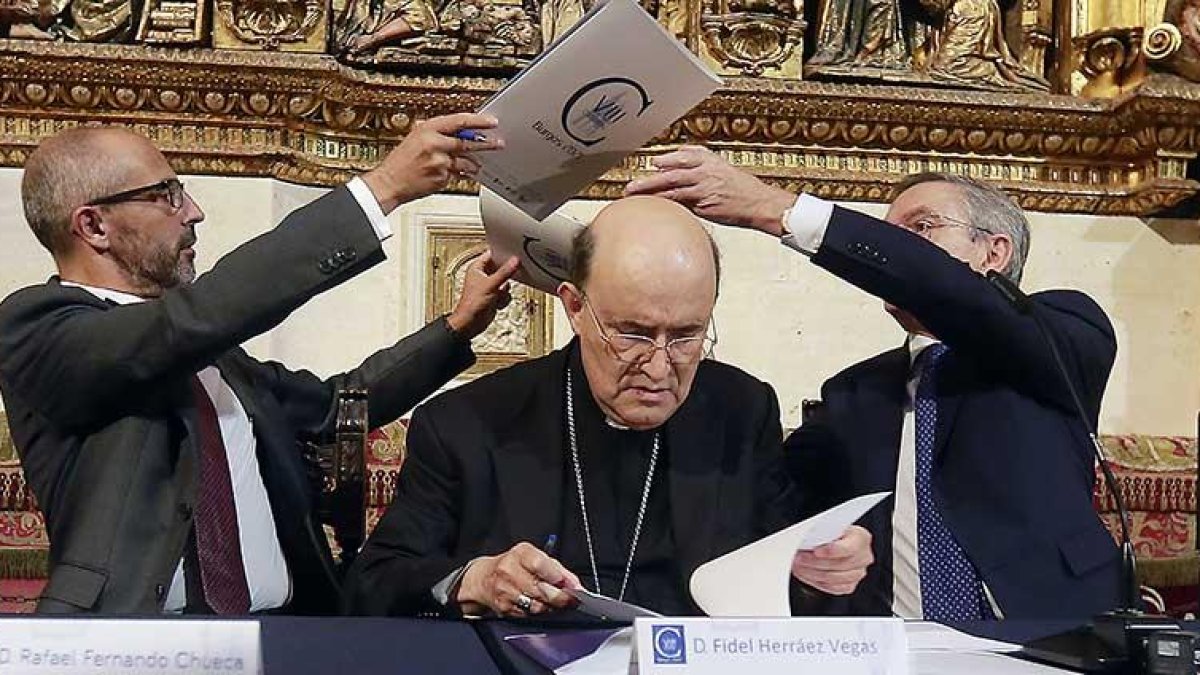 Rafael Fernando Chueca, de ‘la Caixa’, intercambia el convenio con Ginés Clemente, de Caja de Burgos. Entre ellos el arzobispo Fidel Herráez.-RAÚL G. OCHOA