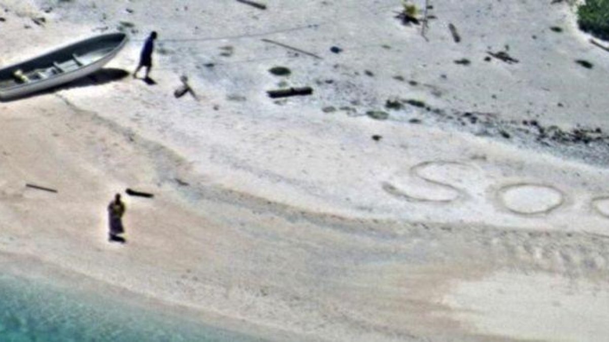 SOS escrito en la arena de playa por Linus y Sabina Jack.-US NAVY