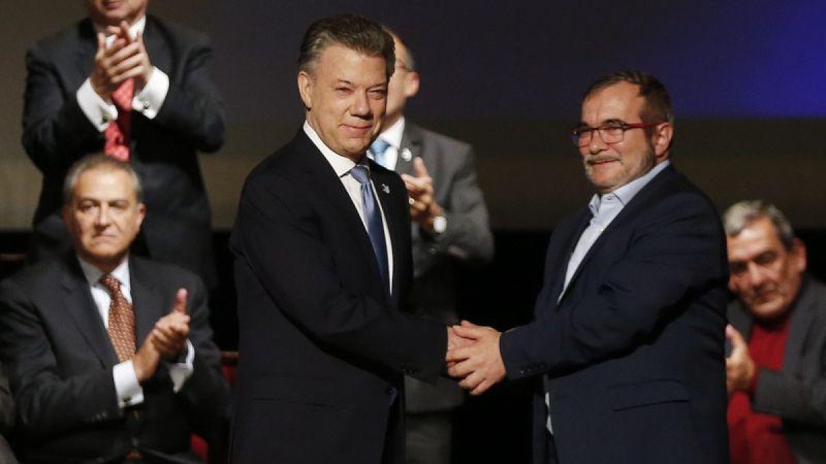 Santos (izquierda) y Rodrigo Londoño, alias 'Timochenko', se dan la mano tras firmar el nuevo acuerdo, en Bogotá, este jueves.-AP / FERNANDO VERGARA