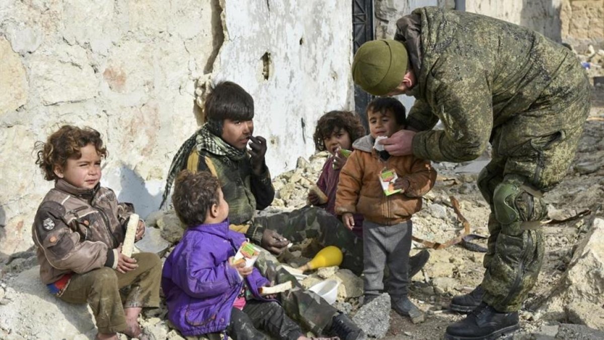 Un militar ruso entrega supuestamente zumo de frutas a niños de Alepo (Siria), en una imagen sin fecha distribuida por el Ministerio de Defensa ruso.-/ AP