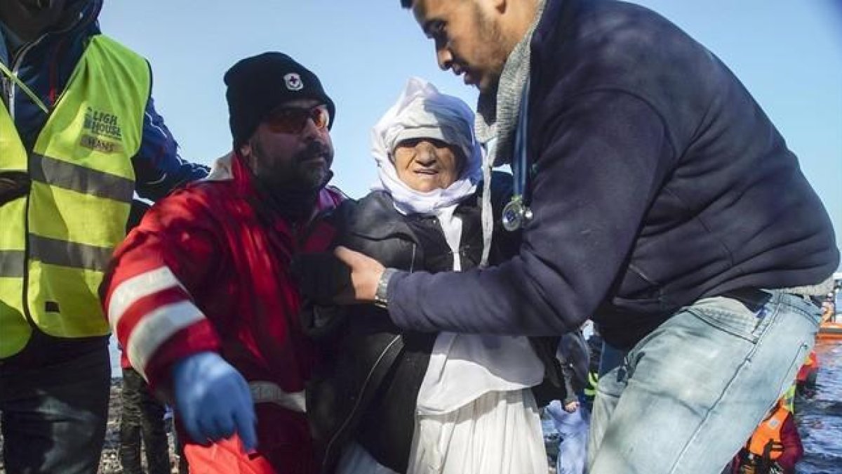 Voluntarios ayudan a una mujer anciana de Afganistán tras desembarcar con otros refugiados en Skala Sykaminias, en Lesbos, este miércoles.-AP / MSTYSLAV CHERNOV